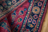 Textured detail of a Sarouk rug's cranberry field and stylized navy floral border.