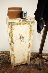 Vintage industrial cabinet with chippy paint and floral details in a styled vignette.