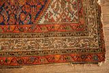 Tattered corner of a vintage tribal Hamadan rug, showing worn indigo and rust borders.