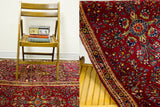 Close-up of the dark red plush Sarouk Persian rug, highlighting intricate floral motifs and curled edge.