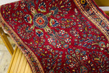 Plush dark red Sarouk rug detail, featuring dense floral motifs and natural side curl.
