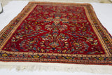 Plush dark red pile featuring intricate floral motifs and soft white fringe on a vintage Sarouk rug.