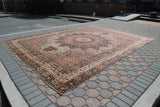 Antique Kerman rug showing sun-like medallion, daisy-filled ivory field, and intricate red floral borders.