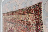 Corner detail of an antique Persian Kerman, with intricate red, ivory, and black floral borders.