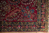 Corner detail of an antique Sarouk showing meandering floral borders in navy blue and gold framing a cherry red field.