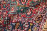 Folded vintage Persian Karaja rug highlighting geometric blossoms, checkered design, cherry red, navy.