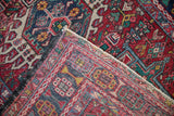 Hand-knotted vintage Karaja rug's folded corner, revealing geometric blossoms, tattered fringe, and foundation weave.