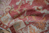 Textured pile of vintage distressed Oushak rug, with varied raspberry and tangerine tones and geometric blossoms.