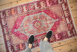 Rich fuchsia, tangerine, and blue floral medallion on distressed vintage Oushak rug.
