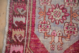 Distressed Oushak rug corner: fuchsia and tangerine floral motifs on a faded blue field, intact selvage.