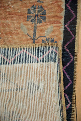 Distressed Oushak rug detail showing pale tangerine geometric pile, navy zig-zag border, and woven foundation.