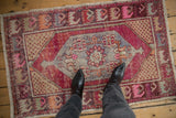 Distressed vintage Oushak rug with central floral medallion, vines, and seed patterns in magenta, blue, beige.