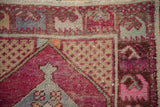 Distressed Oushak rug corner: magenta floral border, beige seed spandrel, and faded blue accents.