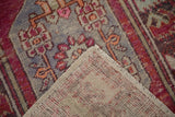 Folded corner of the vintage Oushak rug, showing its distressed magenta and blue floral pile and woven foundation.