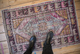 Textured vintage distressed Oushak rug showing worn violet, blue, pink, and gold floral medallion.