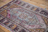 Distressed Oushak rug showing worn pile texture, violet, blue, pink, and gold floral patterns.