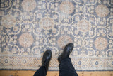 Distressed vintage rug texture with visible knot heads in a denim blue and cream floral pattern.