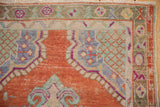 Close-up of the vintage Oushak's worn texture, showing its rust, pale blue, and magenta border.