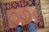 Distressed vintage Oushak rug with worn tomato red pile and navy hook and latch border.