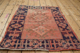 Angled detail of the distressed vintage Oushak rug, showing tomato red field and navy hook and latch border.