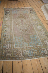 Distressed vintage Oushak rug corner showing textured pile, faded mauve, dusty blue, and green patterns.