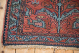Vintage Lilihan rug corner with cherry red field, sky blue serrated leaf border, and tattered end.