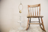 Chippy white Cambridge table lamp stem with floral details, beside a distressed antique chair.