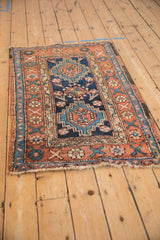 Angled view of an antique Heriz rug featuring a central geometric medallion in indigo, terracotta, and sand.