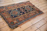 An antique Persian Heriz rug's geometric motifs and low pile in dusty terracotta, indigo, and teal.