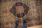 Antique Kermanshah rug's navy medallion edge, ivory floral field, cochineal vines, and even wear.