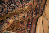 Antique Malayer rug's folded detail, highlighting navy Herati patterns and terracotta banded borders.
