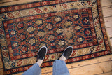 Aged pile texture on a Caucasian rug, showing geometric boteh patterns in blue and red.