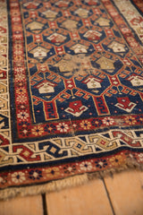 Antique Caucasian rug's worn end, featuring geometric blue, red, ivory motifs and frayed fringe.
