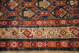 Geometric ivory, red, and blue border with tattered fringe on an antique Caucasian rug.