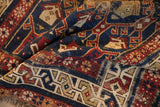 Hand-knotted Caucasian rug detail showing folded pile, geometric boteh motifs in sapphire blue, brick red, and ivory.
