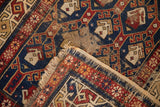 Antique Caucasian rug detail: geometric panels, threadbare pile, exposed foundation, and tattered fringe.