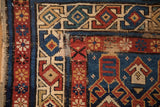Detail of antique Caucasian rug corner, highlighting geometric motifs, exposed foundation, and worn pile.