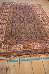 Aged fringe and ornate borders of an antique Malayer rug with raspberry, ivory, and blue.