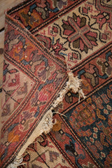 Tattered end and hard loss on an antique Malayer rug with rust, blue, ivory geometric pattern.