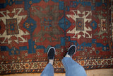Vintage Caucasian rug showcasing geometric patterns in black cherry red, sapphire blue, ivory tones with visible wear.