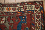 Vintage Caucasian rug corner close-up, geometric star motifs, black cherry red, sapphire blue, and tattered fringe.