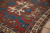 Vintage Caucasian rug's geometric patterns in sapphire blue, black cherry red, ivory with tattered fringe.