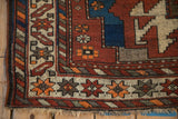 Tattered fringe and geometric pinwheel motifs on a vintage Caucasian rug corner.