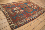 Vintage Caucasian rug corner detail: geometric border, red, blue, ivory, and visible tatter.