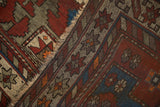 Close-up of vintage Caucasian rug with geometric patterns, tattered fringe, in black cherry, sapphire blue, and ivory.