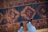Antique Caucasian runner, worn navy and black cherry red geometric patterns, threadbare, feet in view.