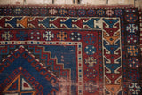 Antique Caucasian rug edge with red, navy, and ivory geometric patterns and worn fringe.