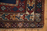 Collector antique Caucasian rug detail showing geometric navy, red, ivory patterns, visible wear, and fringe.