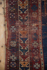 Antique Caucasian runner with visible foundation, tattered side, and geometric red, blue, ivory motifs.