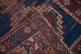 Folded antique Caucasian runner corner reveals geometric navy, red, ivory patterns, and tattered fringe.
